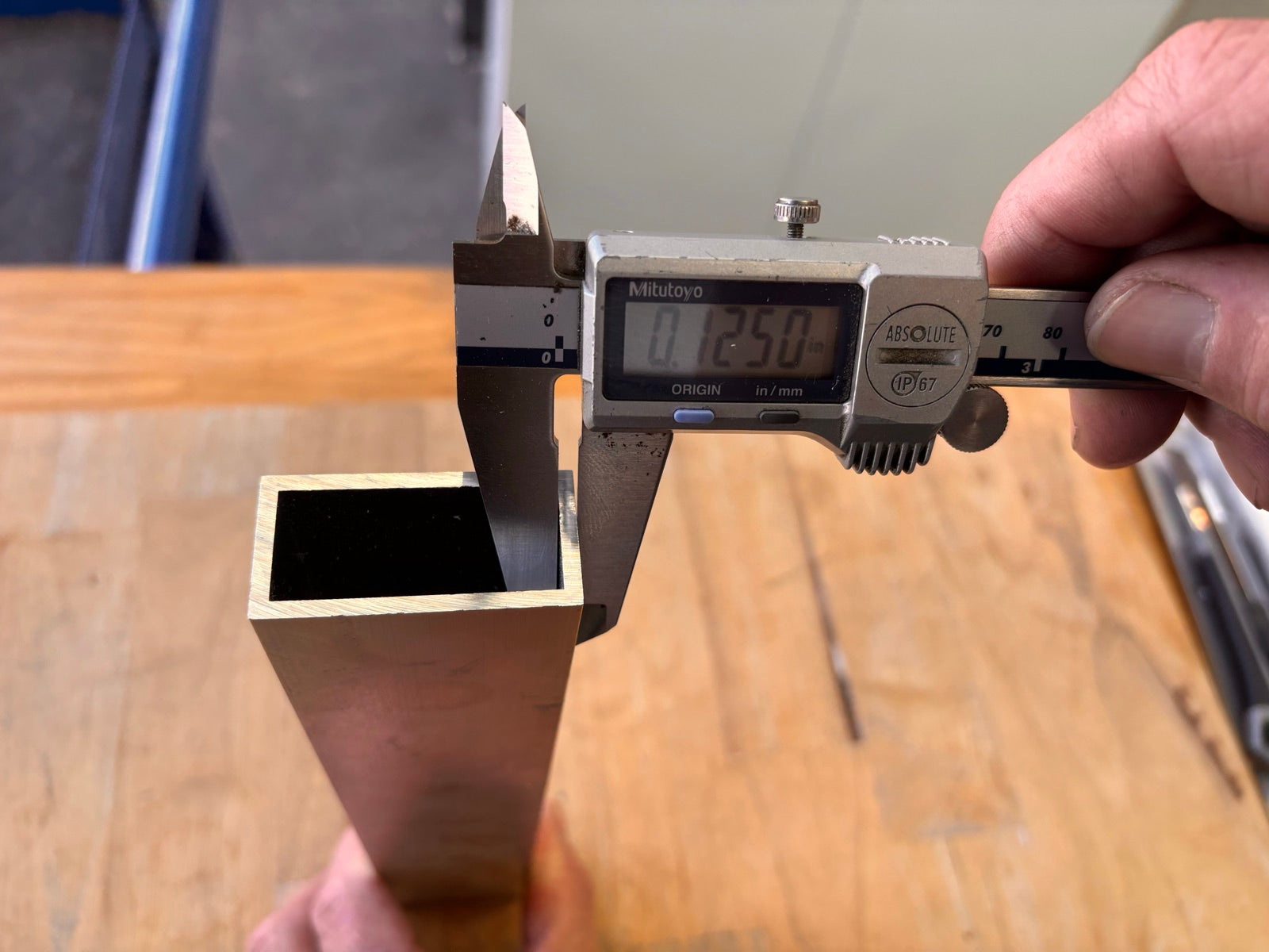 Digital calipers measuring a square aluminum tube with aluminum end caps nearby.