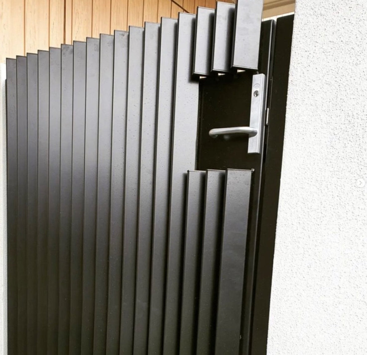 Black aluminum pedestrian gate with square end caps fitted into vertical battens.