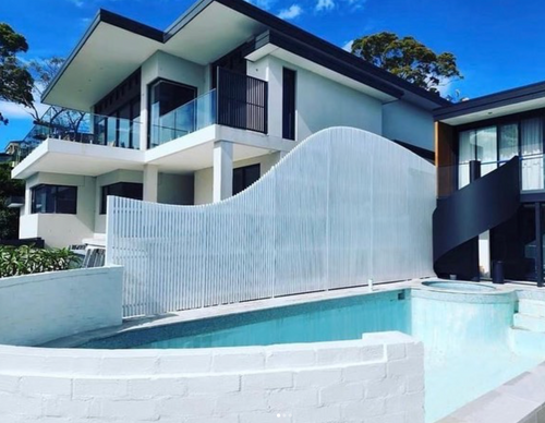 Modern house with a pool and white aluminum fence under a blue sky.