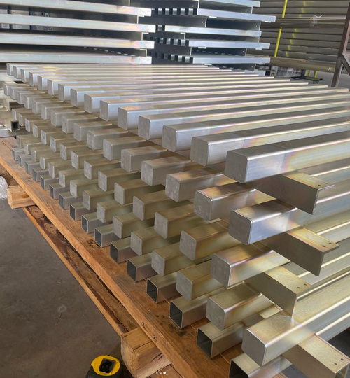 Stacks of aluminum rectangular bars on a wooden pallet in an industrial setting