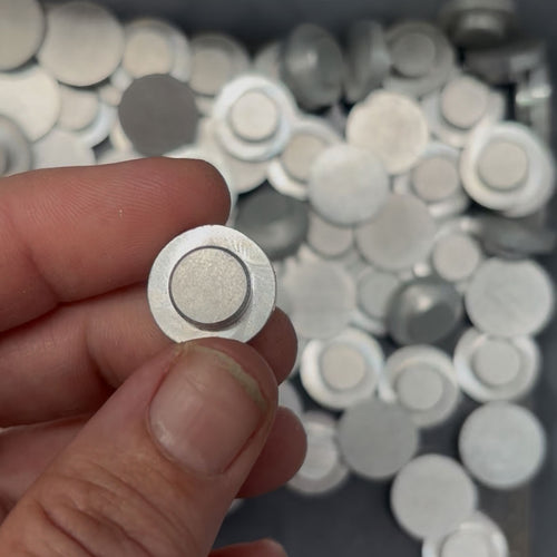 Hand holding a small round aluminum end cap with a blurred background of similar end caps.