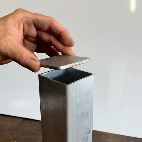 Hand placing a aluminum end cap onto a aluminum tube with a white background