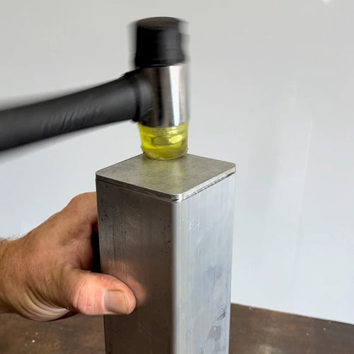 Black and yellow rubber mallet striking a aluminum end cap into a aluminium tube. 