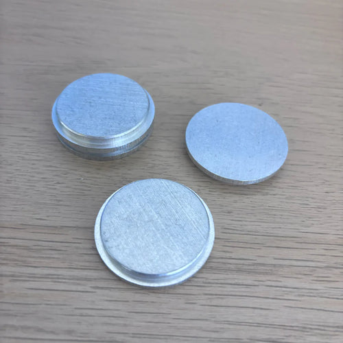 Three round aluminum end caps on a wooden surface