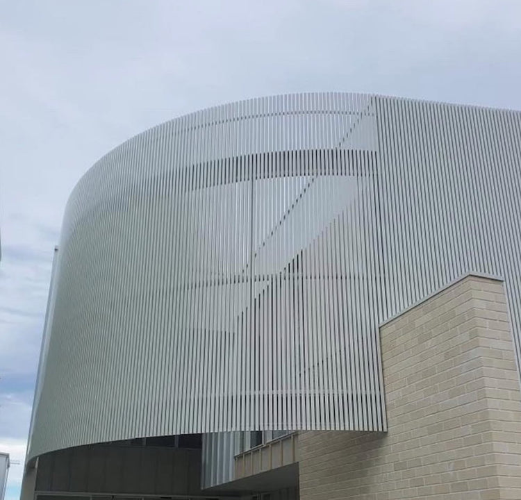 Curved architectural aluminum facade with vertical battens capped using CNC-machined aluminum end caps.