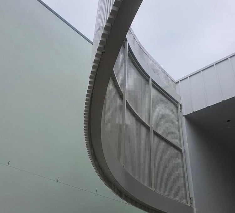 Curved aluminum screening with vertical battens and aluminum end caps fitted on an architectural facade.