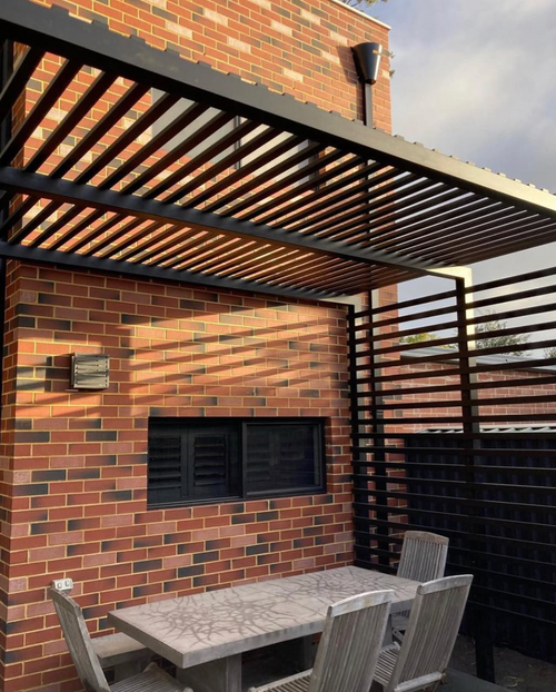 Outdoor patio area with brick wall, aluminum pergola, and dining table with chairs.